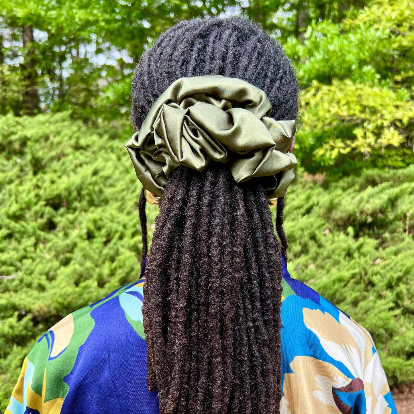 Person with hair in locs wearing a green scrunchie outdoors.